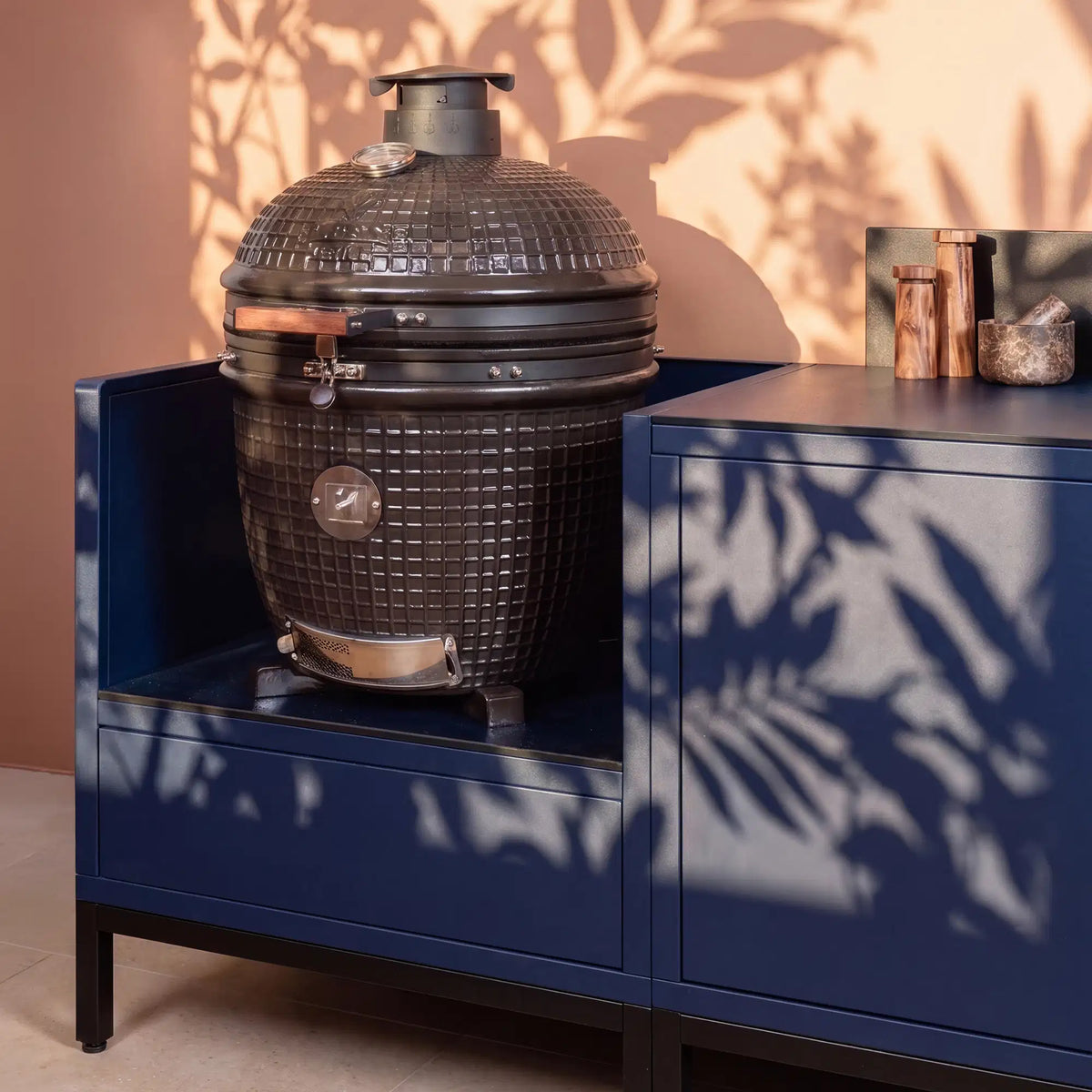 Cuisine extérieure Pilotis bleu marine avec module kamado et plan de travail en céramique noir.
::visuel:noir