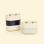 Bougies Totem S Beige ivoire – Citronnelle & Citron, Bleu marine – Citronnelle & Sel de mer et Vert d’eau – Citronnelle & Eucalyptus, deux bougies ovales à double mèche en bois, posées sur un fond beige clair. ::visuel:citron,sel,eucalyptus