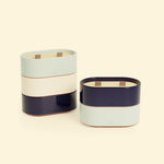 Bougies Totem S Bleu marine – Citronnelle & Sel de mer et Vert d’eau – Citronnelle & Eucalyptus, deux bougies ovales à double mèche en bois, posées sur un fond beige clair. ::visuel:citron
