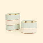 Bougies Totem S Vert d’eau – Citronnelle & Eucalyptus et Beige ivoire – Citronnelle & Citron, deux bougies ovales à double mèche en bois, posées sur un fond beige clair. ::visuel:citron