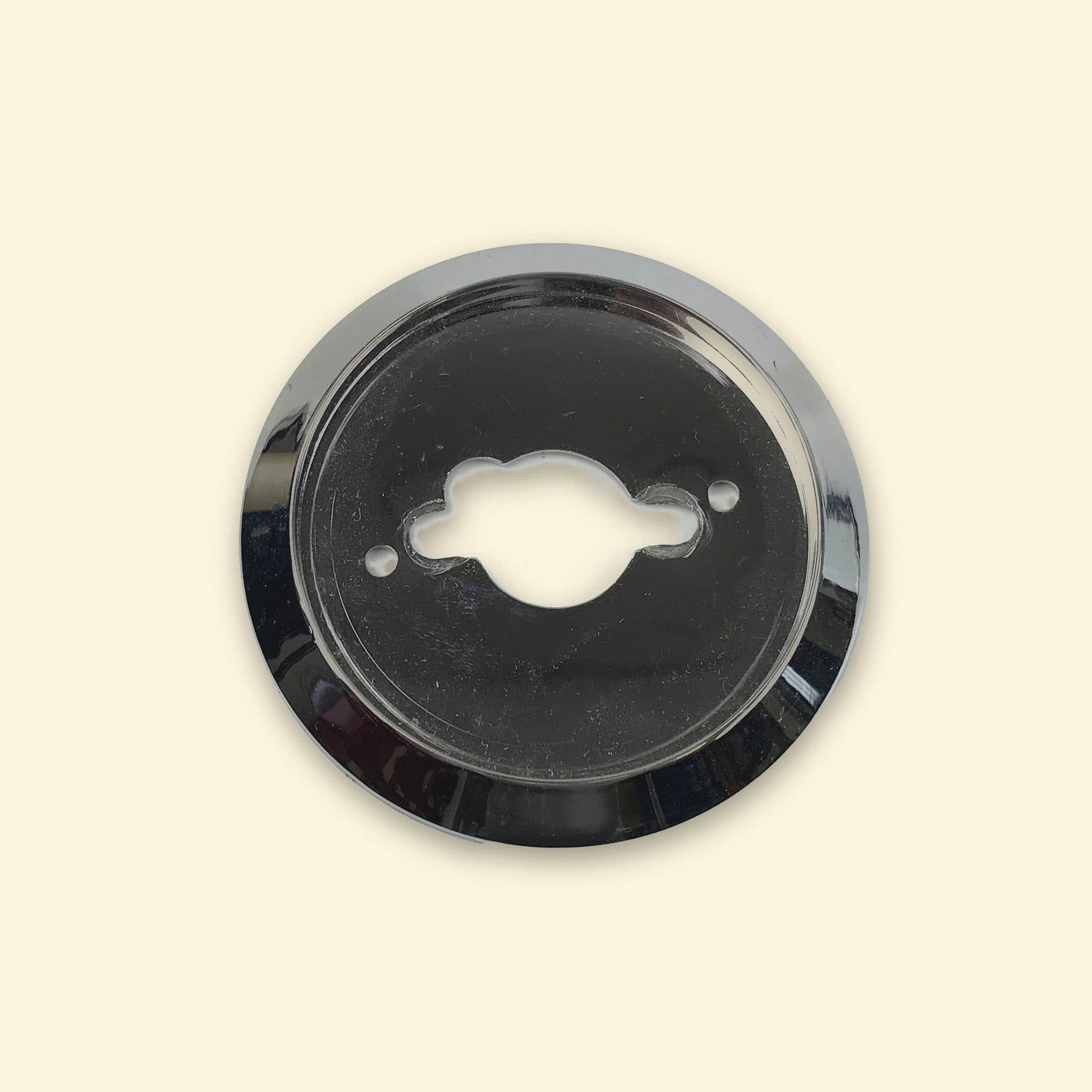 Contour de bouton chromé pour plancha gaz Vivaplancha, pièce ronde vue de face sur fond beige.