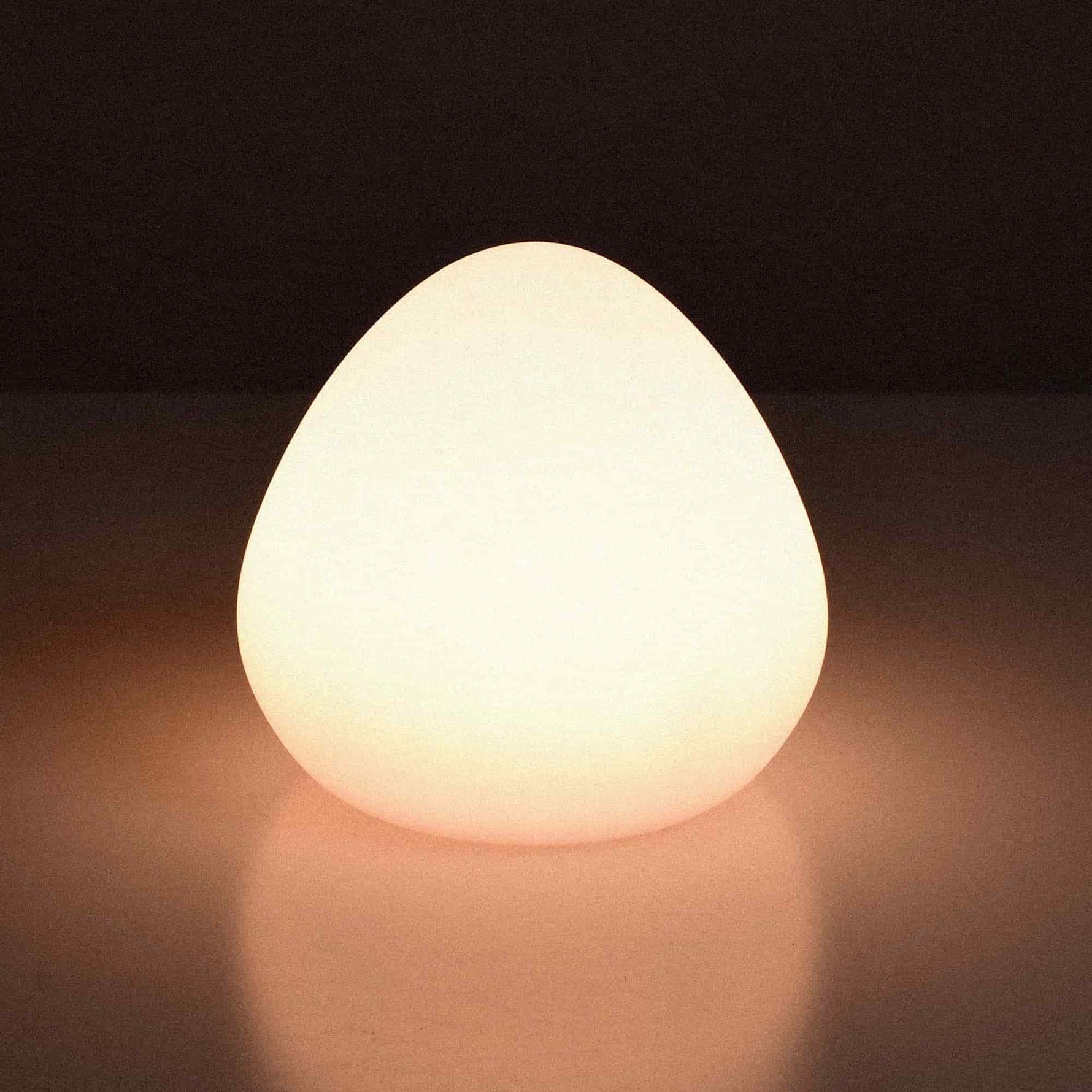 Lampe solaire d’extérieur en forme de noisette, allumée et diffusant une lumière chaude et douce sur une surface claire.